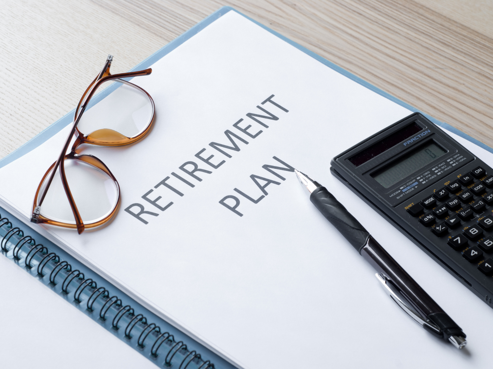 Retirement plan document on a desk with eyeglasses, a calculator, and a black pen.